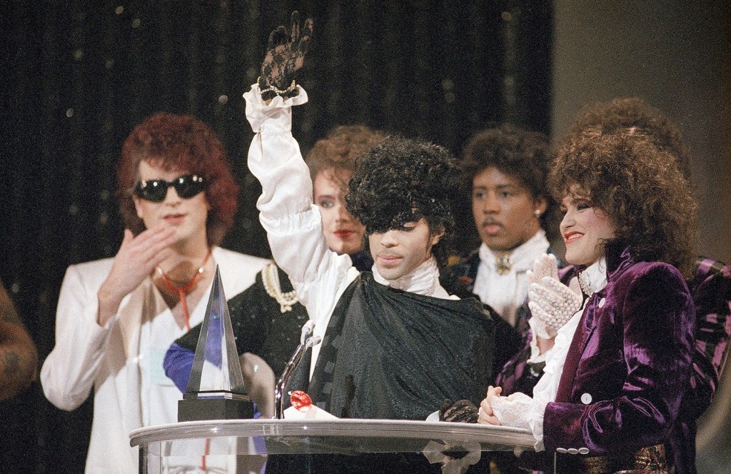 Prince holds up a gloved hand as he accepts an American Music Award for his single “When Doves Cry,” alongside members of his band